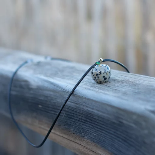 collier pomme en jaspe dalmatien, posé sur une rembarde en bois